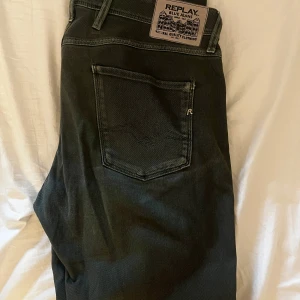 Replay Anbass svarta jeans W34 L32 - Snygga svarta Replay Anbass jeans med klassisk femficksdesign och diskret Replay-logga på fickan. Jeansen har en rak passform och är tillverkade i ett mjukt bomullsmaterial med lite stretch för extra komfort.