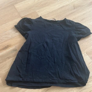 Svart puffärmad topp från 151 - En svart topp från 151 med puffiga korta ärmar och rund halsringning. Tillverkad i mjuk bomull, perfekt för en chill och enkel look. Passformen är normal och toppen är helt enfärgad utan mönster eller detaljer.