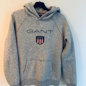 Grå hoodie från GANT  - Snygg grå hoodie från GANT med broderad logga och sköld på bröstet. 