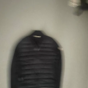 Svart Moncler pufferjacka med dragkedja - Snygg svart pufferjacka från Moncler med quiltad framsida och ärmar i mjukt material. Jackan har två dragkedjefickor och klassisk Moncler-logga på ärmen. Perfekt för dig som vill ha en stilren och sportig look.