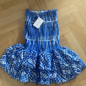 Blåvit kortklänning från Design by Amor - Supersöt kortklänning i blått och vitt från Design by Amor. Klänningen har smockad överdel, aldrig använt 