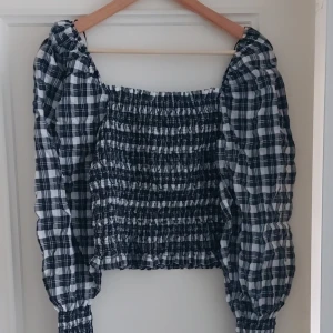 Rutig blus med puffärmar från H&M  - Supersöt rutig blus i svart och vitt med smockad kropp och långa puffärmar. Fyrkantig ringning och elastiska muddar vid ärmslut. Perfekt att styla med jeans eller kjol för en trendig look.