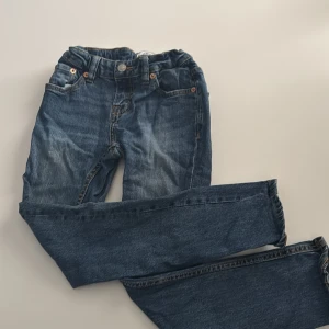 Blå jeansbyxor från 157, stl 140 - Snygga blå jeansbyxor från 157 i modellen Slimmy Star. Klassisk femficksdesign med justerbar resår i midjan och orangea sömmar. Perfekta för dig som gillar en enkel och stilren look till vardags.