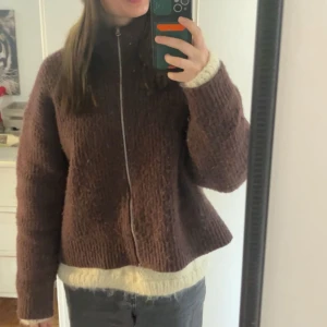 Brun stickad kofta med dragkedja - Mysig brun stickad kofta med dragkedja framtill och hög krage. Koftan har långärmad passform och är perfekt för kyligare dagar. Snygg och enkel att matcha till olika outfits! Köpt från Zalando för 600kr