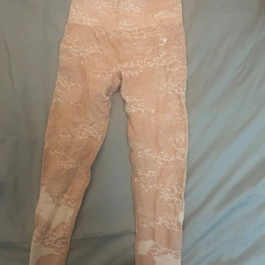 rosa mönstrade leggings från Gymshark - Supersnygga rosa leggings från Gymshark med ljusmönstrat camo-tryck. Hög midja och tight passform, perfekta för gymmet eller chill. Tillverkade i mjuk och stretchig polyesterblandning som sitter skönt hela dagen.