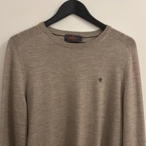 Beige merinoullströja från Morris - Snygg beige stickad tröja från Morris i 100% merinoull. Klassisk rund halsringning och diskret broderad logga på bröstet. Perfekt för lager-på-lager och passar till allt. Stilren och enkel design med lång ärm.