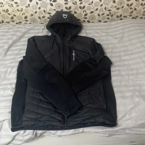 Svart quiltad jacka från Six Deuce - Svart jacka från sail racing med luva och quiltade partier på både fram- och baksida. Jackan har dragkedja framtill, en bröstficka med logga och är tillverkad i syntetmaterial. Perfekt för dig som gillar 