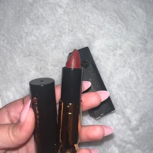 Anastasia Beverly Hills läppstift Heathers - Mörkrött läppstift i nyansen Heathers från Anastasia Beverly Hills. Kommer i en elegant svart och guldig hylsa. Läppstiftet har en krämig formula och ger en djup, vampy look med lätt glans. Perfekt för dig som vill ha en statement-färg på läpparna.