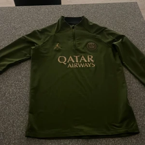 Grön PSG x Jordan långärmad fotbollströja - Snygg grön långärmad fotbollströja från PSG x Jordan med guldfärgade detaljer och Qatar Airways-tryck på bröstet. Slim fit-modell i mjukt, tekniskt material som andas. Perfekt för dig som vill sticka ut på planen eller på läktaren. Mycket skönt när du spelar eller har på dig den 