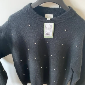 Svart stickad tröja  H&M - Helt oanvänd (prislappen kvar) svart stickad tröja från H&M med rund halsringning och långa ärmar. Tröjan är dekorerad med små diamantliknandr stenar  över hela framsidan för en extra snygg touch. Perfekt nu när det börjar bli lite kallare!