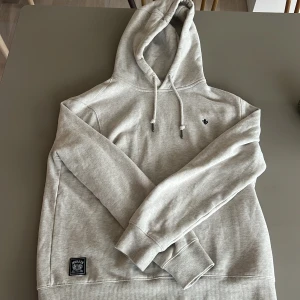 LjusBeige hoodie från Morris - Snygg ljusbeige hoodie från Morris med broderad logga på bröstet. Skulle säga att den sitter bra på någon som är 180 cm