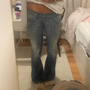 Blå bootcut jeans från Diesel - Snygga blå bootcut jeans från Diesel med slitningar på benen och lätt tvättad look. Låg midja och klassiska fem fickor. Jeansen har en bredare benslut och är tillverkade i jeansmaterial. Perfekta för dig som gillar en avslappnad och trendig stil. Har lite små defekter på utsydning men inga fläckar💗
