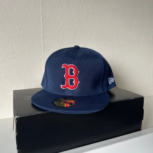 Boston Red Sox keps New Era 59FIFTY - Snygg marinblå Boston Red Sox keps från New Era 59FIFTY med röd broderad B-logga framtill och MLB-logga bak. Klassisk flat peak och strukturerad passform. Materialmix av ull och akryl. Perfekt för dig som vill ha sportig streetstyle.