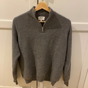 Grå kashmirtröja med half zip Soft Goat - Mysig grå stickad tröja från Soft Goat i 100% kashmir. Tröjan har en hög krage med half zip-dragkedja och ribbade muddar vid ärmslut och nederkant. Perfekt för dig som gillar stilren och klassisk look.