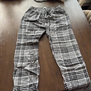 Rutig gråsvart mjukisbyxa stl L - Mysiga mjukisbyxor i grått och svart med rutigt mönster. Byxorna har resår i midjan och snörning för extra komfort. Perfekta för chill dagar hemma eller när du vill vara bekväm. Tillverkade i mjukt material som känns skönt mot huden.