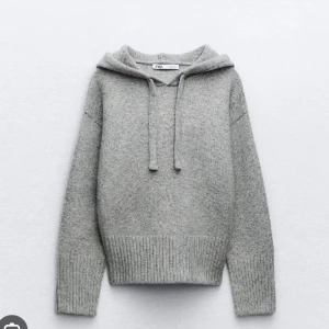 Grå stickad hoodie från Zara - Mysig grå stickad hoodie från Zara med huva och snörning. Tröjan har långa ärmar och breda ribbade muddar vid ärmslut och nederkant. Perfekt för kyliga dagar och enkel att matcha med jeans eller mjukisbyxor.