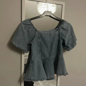 Blå jeansblus med puffärm från H&M - Supersöt blå jeansblus från H&M med puffiga korta ärmar och volang nertill. Strl 134/140 men skulle säga att den sitter som en xs.