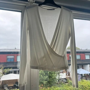 Vit omlottopp från NA-KD XS - Säljer en stilren vit omlottopp från NA-KD i storlek XS. Toppen har lång ärm, djup v-ringning och är tillverkad i mjuk viskosblandning med stretch. Perfekt för en clean och fräsch look med snygg omlottdetalj framtill.
