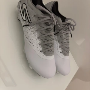Gråvita fotbollsskor från Skechers SG dubbar  - Ett par helt nya fotbollsskor helt oanvända och riktigt bra skick, har storleken 42,5 men sitter tajtare i bredden. Det är SG dubbar {skruv} som man ser så finns inga till dem, tappat bort dem men finns att köpa separat endast för 199 kr därför blir priset 1199:- men ord: pris 1599:- på nätet!!👍