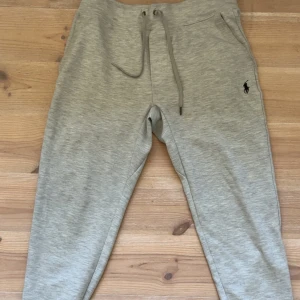 Grå mjukisbyxor från Polo Ralph Lauren - Snygga ljusgrå mjukisbyxor från Polo Ralph Lauren med klassisk broderad logga på benet. Byxorna har dragsko i midjan och är tillverkade i mjukt bomullsmaterial. Perfekta för en chill och avslappnad stil.