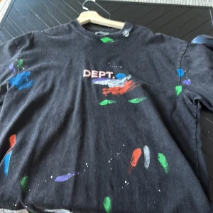 Svart t-shirt från DEPT med färgstänk - Cool svart t-shirt från DEPT med tryck framtill och färgstänk i blått, grönt, rött, lila och vitt. T-shirten har rund hals och korta ärmar, perfekt för dig som gillar streetstyle och unika detaljer.