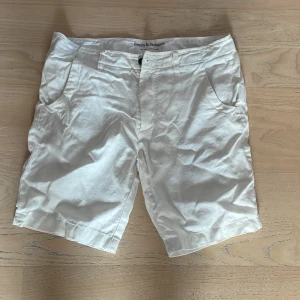 Vita linneshorts från Bruun & Stengade - Snygga vita shorts från Bruun & Stengade i skönt linnematerial. Klassisk passform med fickor på sidorna och hällor för bälte. Perfekta för varma sommardagar och ger en fräsch och stilren look.