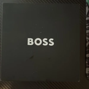 Guldig BOSS kronografklocka meshband - Snygg klocka från Hugo Boss med guldig mesh-länk och svart urtavla. Klockan har kronograf, datumvisning och tydliga indexmarkeringar. Stilig design med robust känsla och detaljer i guld. Levereras i originalask med manual.