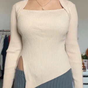 Beige ribbad bolerotopp med slits - Trendig beige bolerotopp med lång ärm och ribbad struktur. Toppen har en fyrkantig urringning och en snygg asymmetrisk slits på ena sidan. Perfekt för dig som gillar unika detaljer och en stilren look. Alltid välkommen att ställa frågor!