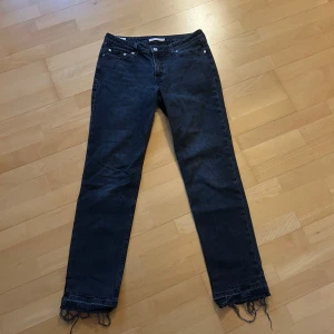 Levi's svarta straight jeans med råa kanter - Svarta Levi's jeans i modellen Low Pitch Straight med klassisk femficksdesign och raka ben. Jeansen har låg midja och råa, fransiga benslut för en cool, avslappnad look. Tillverkade i slitstarkt denimtyg. Perfekta för dig som gillar en tidlös men edgy stil.