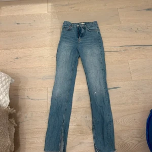 Blå jeans med slits och rå kant - Snygga blå jeans från Gina Tricot med hög midja och raka ben. Jeansen har slitsar nertill och råa kanter för en trendig look. Klassisk femficksmodell i denim med ljus tvätt och knappgylf. Perfekta för dig som gillar en avslappnad men stilren vibe. Väldigt långa, 170-175 cm.  Storlek 34 men känns som 36/S. Ett litet hål på vänstra sidan då det följde med när jag köpte dem. 