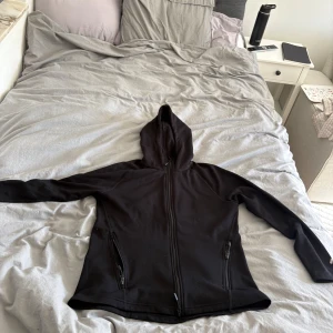 Svart hoodie med dragkedja och huva - Svart hoodie med hel dragkedja framtill och två fickor med dragkedja. Tröjan har huva och är långärmad, perfekt för lager-på-lager. Materialet känns mjukt och bekvämt, troligen bomull eller polyester. Enkel och stilren design som funkar till det mesta. Storlek L från lager 157