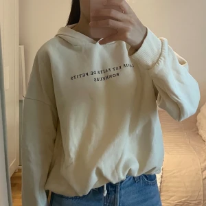 Beige hoodie med tryck och snörning - Säljer en beige hoodie med svart texttryck på bröstet. Tröjan har huva, långa ärmar och snörning i nederkanten för justerbar passform. Perfekt för en chill och avslappnad stil. Materialet känns mjukt och skönt, troligtvis bomull eller bomullsblandning.