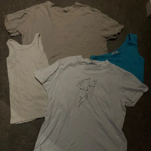 Vit t-shirts och linnen - Vit t-shirt från NA-KD med minimalistiskt svart tryck av två kroppar på bröstet. Sedan en beige t shirt. Sen har vi två linnen, ett vitt och ett blått med endast en arm. Den blå är aldrig använd, och har prislapp kvar. Tänkte antingen sälja allt för 80kr men kan sälja enskilt med för en liten summa. 