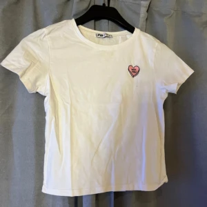 Vit t-shirt med hjärtdetalj FB Sister - Vit t-shirt från FB Sister i bomull med korta ärmar och en liten rosa hjärtpatch på bröstet där det står 'Not You'. Enkel och clean design med normal passform, perfekt till jeans eller kjol.