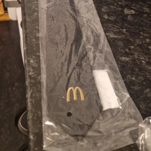 Svart slips McDonald's  - Svart slips från Bernhardtz med McDonald's klassiska gula logga broderad längst ner. Tillverkad i en mix av polyester och bomull, perfekt för dig som vill ha en unik accessoar med snabbmatsvibbar.