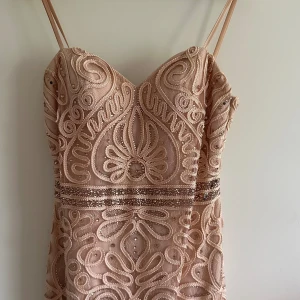 Klänning - Superfin kort klänning i champagnefärg med tunna axelband och v-ringning. Klänningen har ett detaljerat broderat mönster med paljetter och pärlor som ger en glittrig känsla. Materialet är lätt och känns lyxigt, perfekt för dig som vill sticka ut.