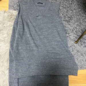 Grå stickad långklänning Made in Italy - Snygg grå stickad långklänning med v-ringning och ärmlös design. Klänningen har bred ribbad kant nedtill och runt halsen, vilket ger en cool och avslappnad look. Perfekt för lager-på-lager-stil under kallare dagar.