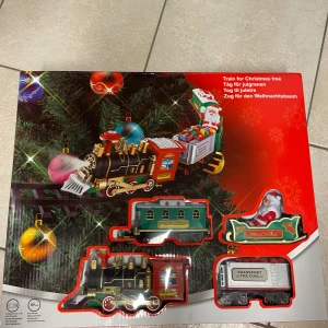 Train for Christmas tree - Elektriskt tågset för julgranen med klassisk design, inklusive lok, vagnar och jultomte. Perfekt för att skapa en festlig stämning runt granen. Produkten är ny i förpackning och passar som dekoration eller leksak under julen.