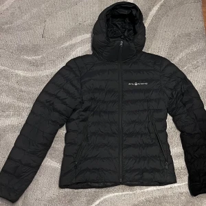 Svart dunjacka från Sail Racing M - Säljer en svart dunjacka från Sail Racing i storlek medium. Jackan har huva och två fickor med dragkedja. Köpt för 3 199kr, är i väldigt bra skick. 
