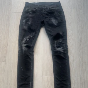 Svarta Dondup Jeans  - Svarta skinny jeans från Dondup i modellen George med slitna detaljer och färgstänk för en edgy look. Jeansen har klassisk femficksdesign, låg midja och smal passform. Perfekta för dig som gillar streetstyle och vill sticka ut lite extra.