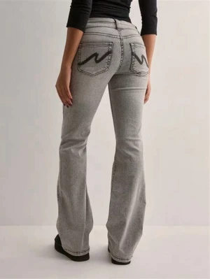 Nelly grå bootcut jeans - Snygga grå bootcut jeans med svarta broderier på bakfickorna. Jeansen har låg midja och klassisk femficksdesign. Tillverkade i denim med lätt stretch för skön passform. Säljer då jag beställde fel storlek! Endast testat aldrig använt💗