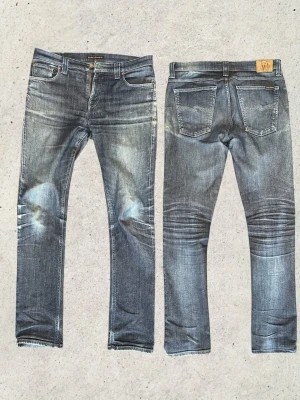 Blå slitna jeans från Nudie Jeans - Riktigt snygga Nudie jeans i slim fit-passform med lite stretch som gör dem bekväma att bära. Storlek W34 L34 med mått: midja 44 cm, längd 110 cm och benöppning 18 cm. Lappen där modellnamnet står är urtvättad, vilket gör att det troligen rör sig om en äldre modell. Har en riktigt snygg colorway samt fades som gör att jeansen sticker ut och ger dem ett sjukt bra helhetsintryck. Vid fler funderingar är det bara att skriva mvh FABIANFASHION