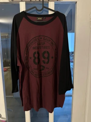 Bordeaux långärmad t-shirt GASP - Snygg långärmad t-shirt från GASP i bordeaux med svarta ärmar och stort tryck framtill. Skön passform och sportig look, perfekt för dig som gillar streetwear. Materialet känns mjukt och bekvämt, troligen bomull. Klassisk rund halsringning.