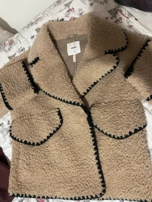 Beige teddyjacka  - Säljer en beige teddyjacka från Object med markerade svarta sömmar. Jackan har stora slag, två fickor framtill och är gjord i ett mjukt, fluffigt material som ger en trendig look. Perfekt för dig som gillar oversized och cozy stil. Köpte för 1200kr och använd endast några gånger!