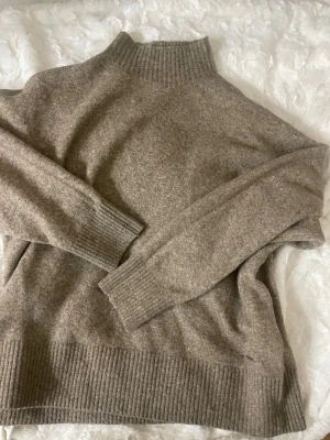 Beige/brun stickad tröja från Everest - Mysig beige stickad tröja från Everest med hög ribbad krage. Tröjan har en avslappnad passform och är tillverkad i ett mjukt material som passar perfekt för kyliga dagar.