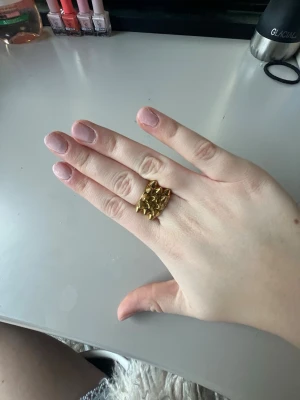 Guldig ring med nitar från Edblad  - Cool guldig ring från Edblad med markerade nitar runt hela ringen. Ringen har en bred design och är tillverkad i metall med en blank finish. Perfekt för dig som vill ha en edgy accessoar som sticker ut.