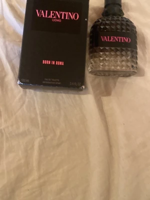Valentino Uomo Born In Roma EdT - Valentino Uomo Born In Roma Eau de Toilette med en snygg, diamantmönstrad glasflaska och svart lock. Flaskan har en cool gradient från mörkt upptill till klart nedtill och etiketten är svart med rosa text. Doften är maskulin och modern. De e cirka 90ml kvar 