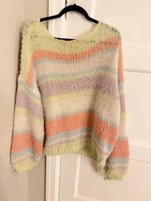 Pastellrandig stickad tröja - Mysig stickad tröja med breda pastellfärgade ränder i ljusgul, persika, lavendel och mintgrön. Tröjan har en lös passform, ballongärmar och ribbstickade muddar. Perfekt för dig som gillar en färgglad och avslappnad stil. Sitter oversized of shoulder jättefin till sommaren 