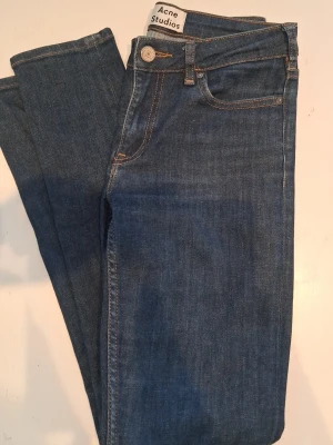 Blå jeans från Acne Studios - Snygga blå jeans från Acne Studios med klassisk femficksmodell och raka ben. Jeansen har orange kontrastsömmar och silverfärgad knapp. Perfekta för en stilren och trendig look.