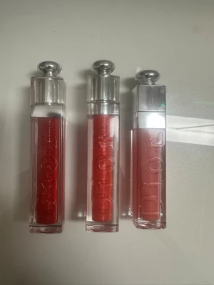 Dior läppglans i röda och rosa nyanser - Tre snygga läppglans från Dior i olika röda och rosa nyanser. De har en stilren fyrkantig förpackning med silverfärgat lock och tydlig Dior-logga på sidan. Perfekt för dig som vill ha glansiga och färgstarka läppar med lyxig känsla. Läppglansen är testade på